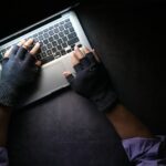 A person wearing fingerless gloves typing on a laptop on a dark surface